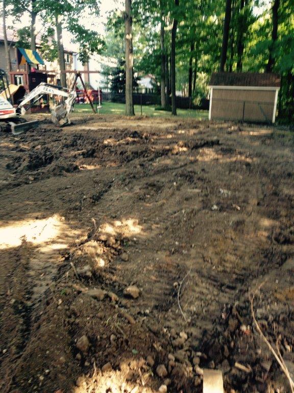 Construction site with muddy dirt ground, trees, and a small shed near a playground area