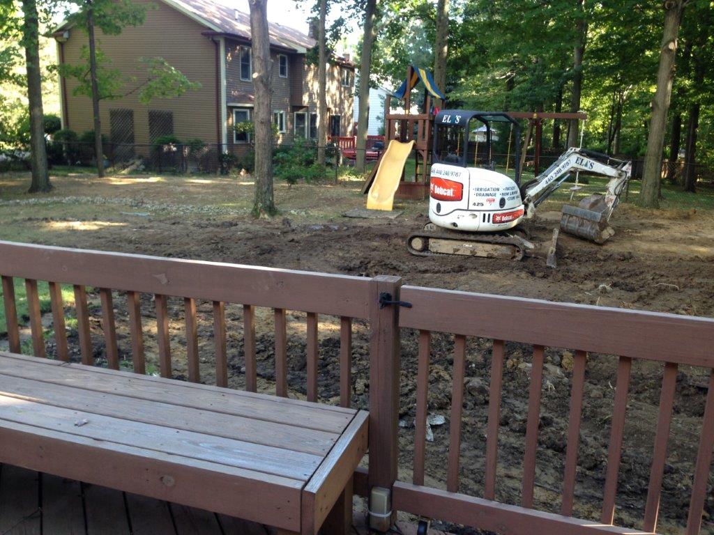 Backyard with deck, trees, playset, and small excavator near a house