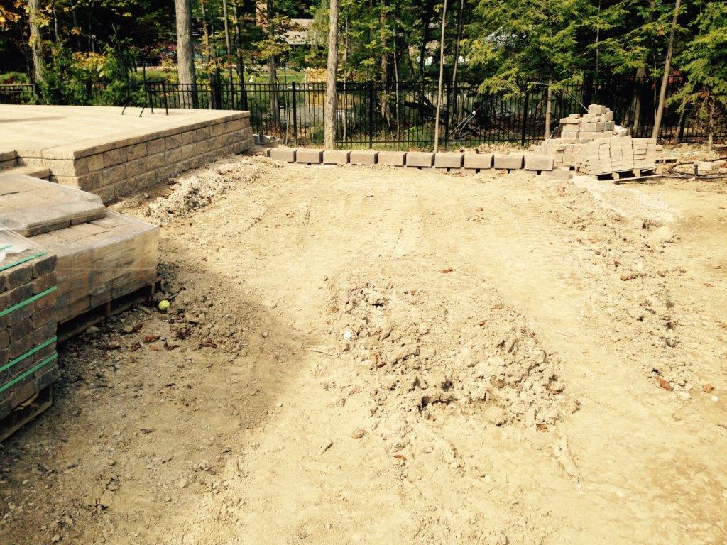 Dirt-covered construction site with stacked bricks on the left and trees in the background