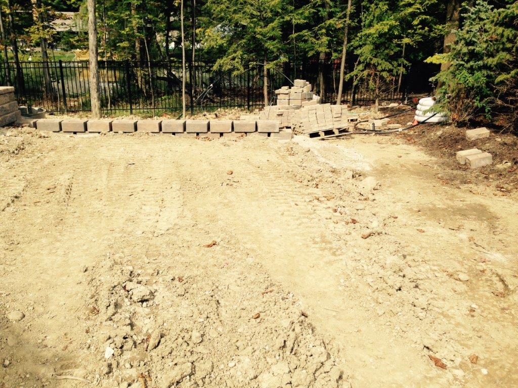 Dirt construction site with a line of concrete blocks in front of a wooded area