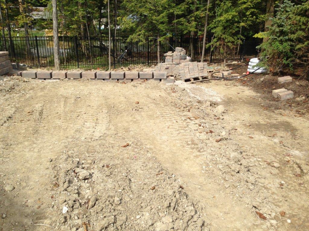 Dirt driveway under construction with stacked stones and trees in the background