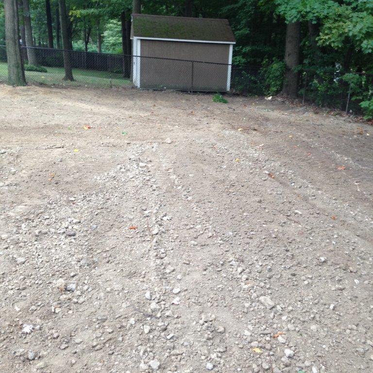 Gravel clearing in a wooded area with a small shed at the back.