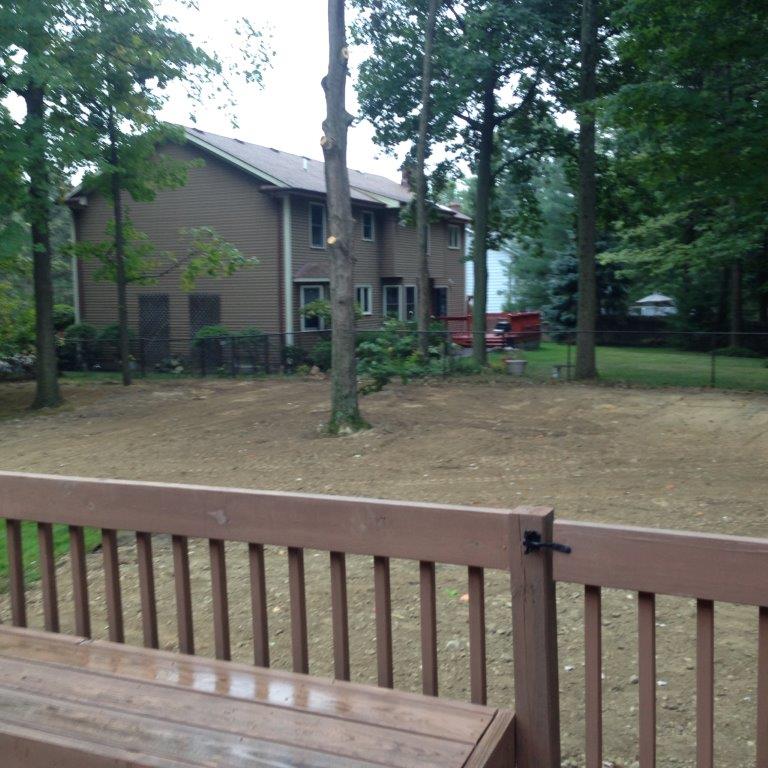 Wooden deck railing overlooking a yard with trees and a brown house in the background