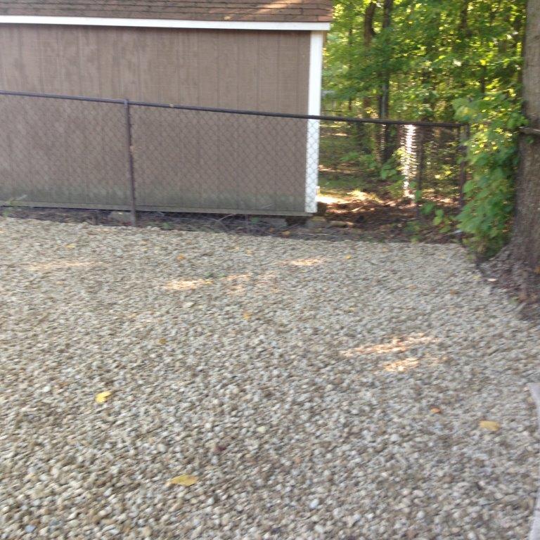 Gravel yard beside a chain-link fence and tan shed, with trees in the background.