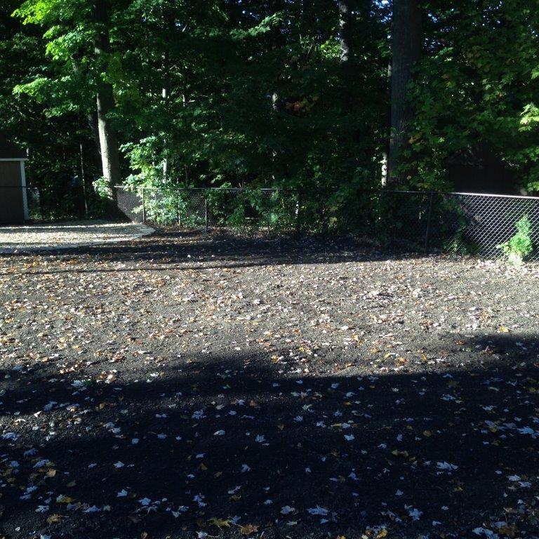 Shaded gravel clearing with trees and a brick wall in the background