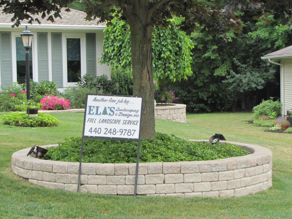 Circular brick planter with a tree and a real estate sign in a front yard