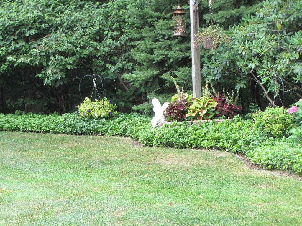 Lawn and garden with dense green trees, flower bed, and a white statue near a pole