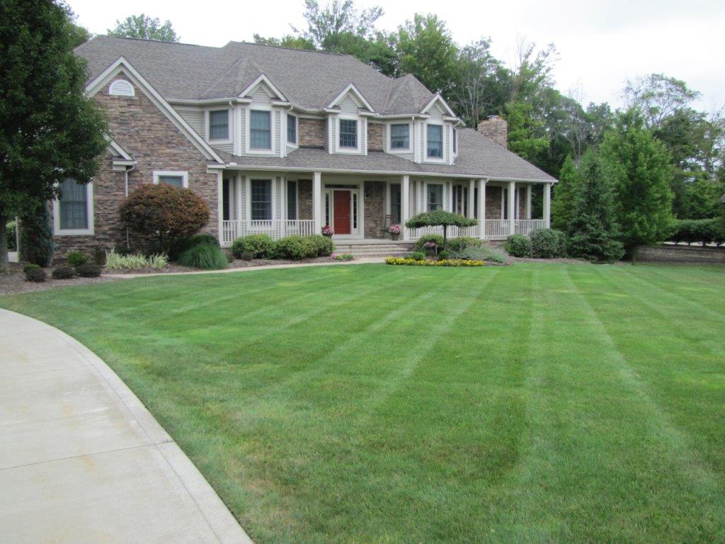 Large two-story suburban house with gray siding, white columns, and a wide green lawn
