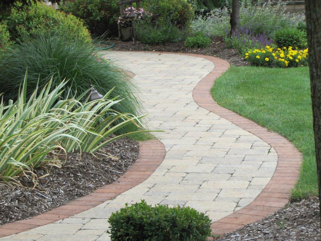 Curved stone garden path bordered by red bricks and green plants
