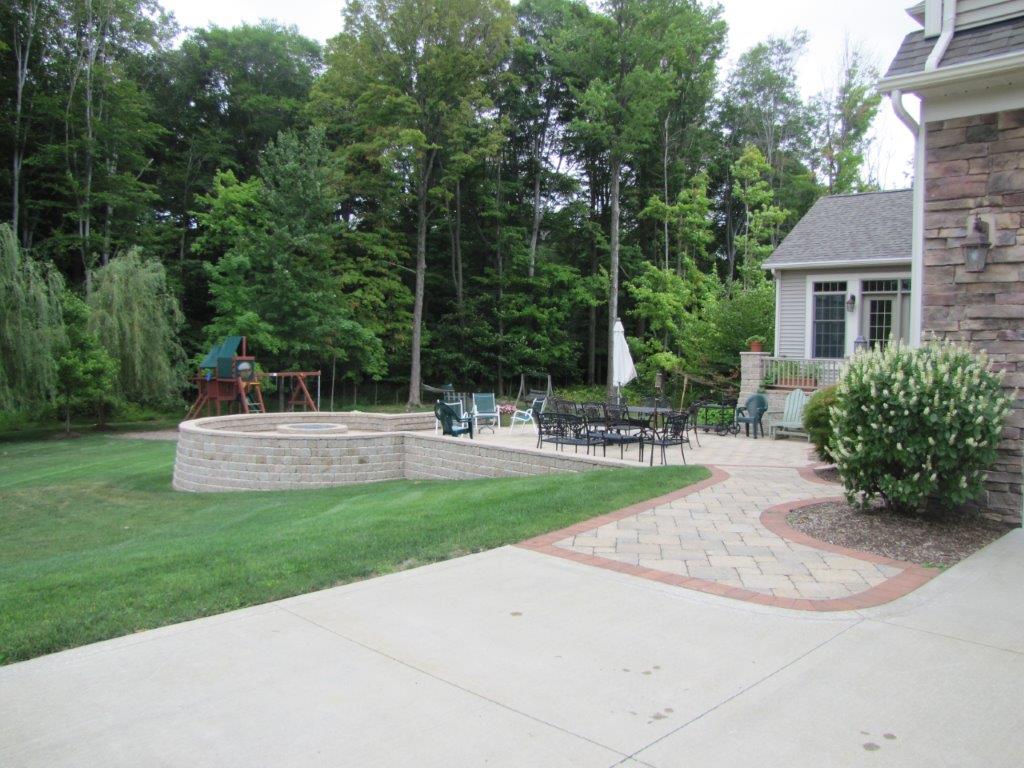 Patio and curved walkway beside a brick house, with outdoor seating and a green lawn.