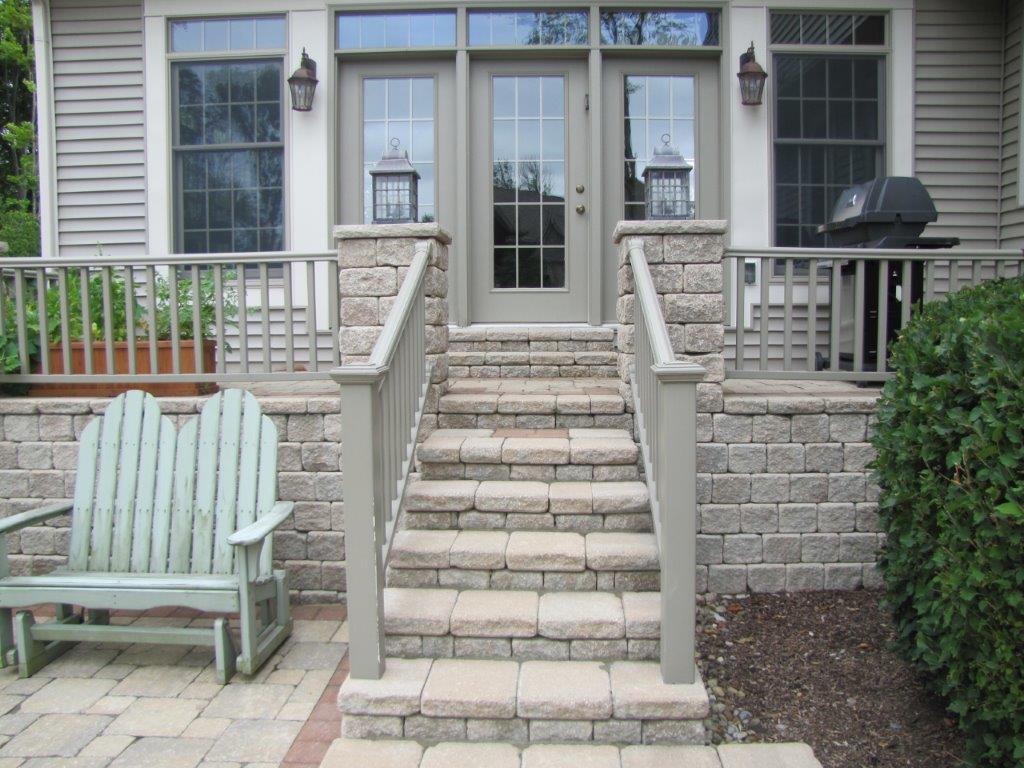 Front steps with stone staircase leading to a house entrance, flanked by railings and a bench on the left.