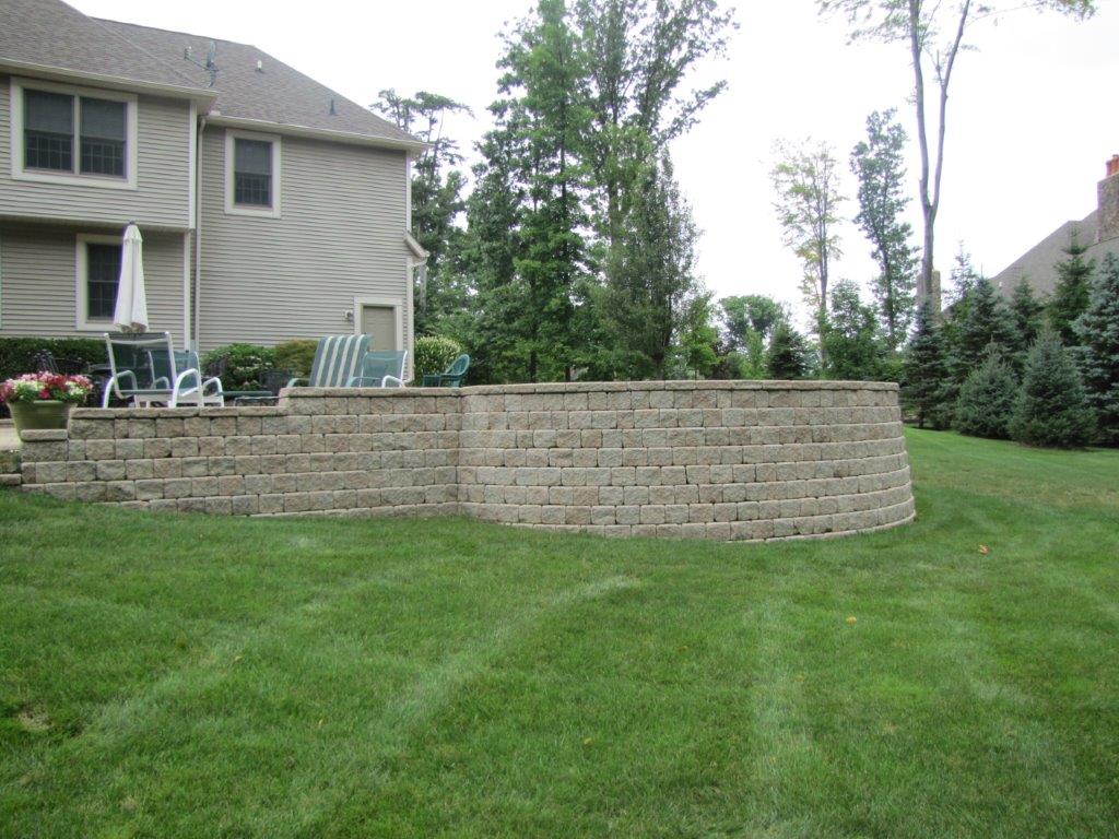 Backyard with a stone retaining wall, green lawn, and house patio