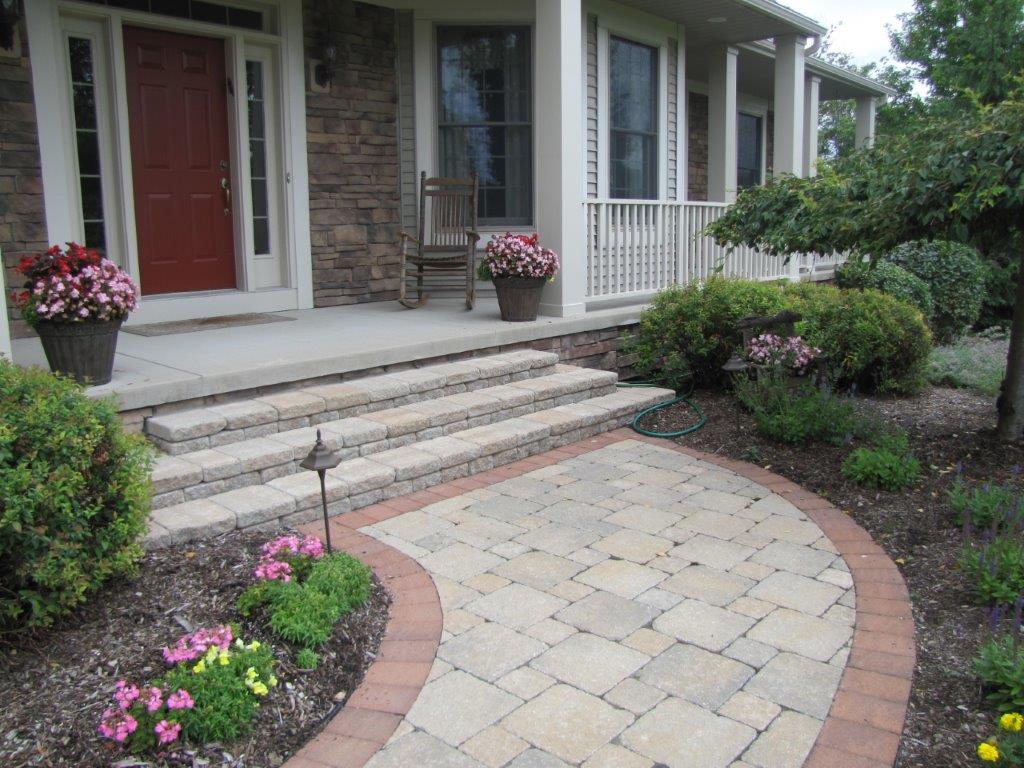 Front porch with stone steps, red door, and curved paver walkway lined with flowers and shrubs