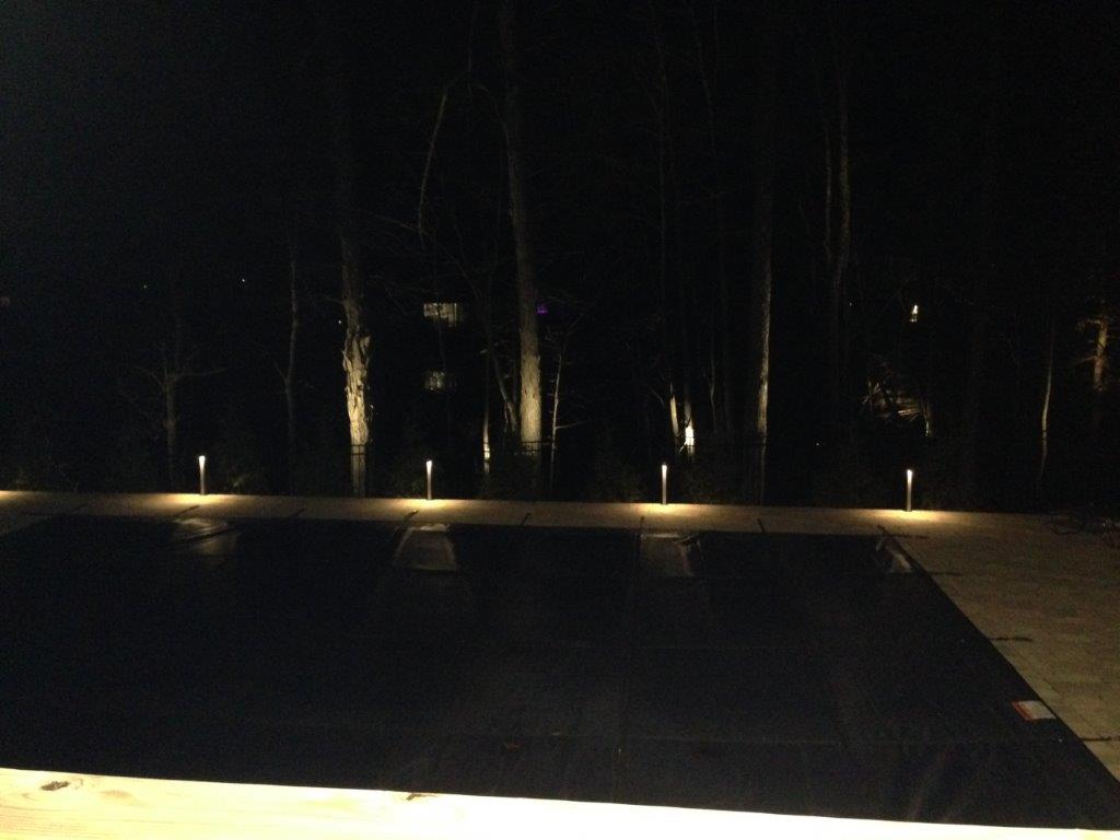 Dimly lit pool at night with small path lights along the edge and trees in the background