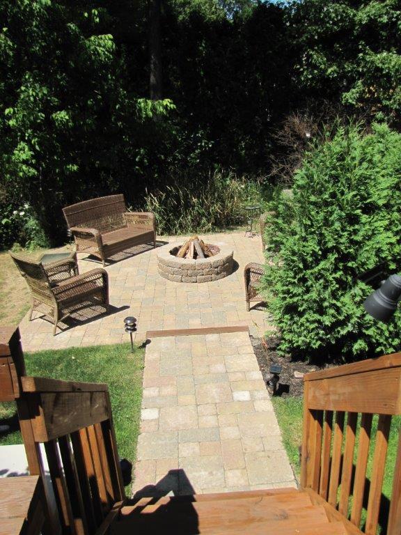 Backyard patio with stone fire pit, benches, and stairs leading down through greenery
