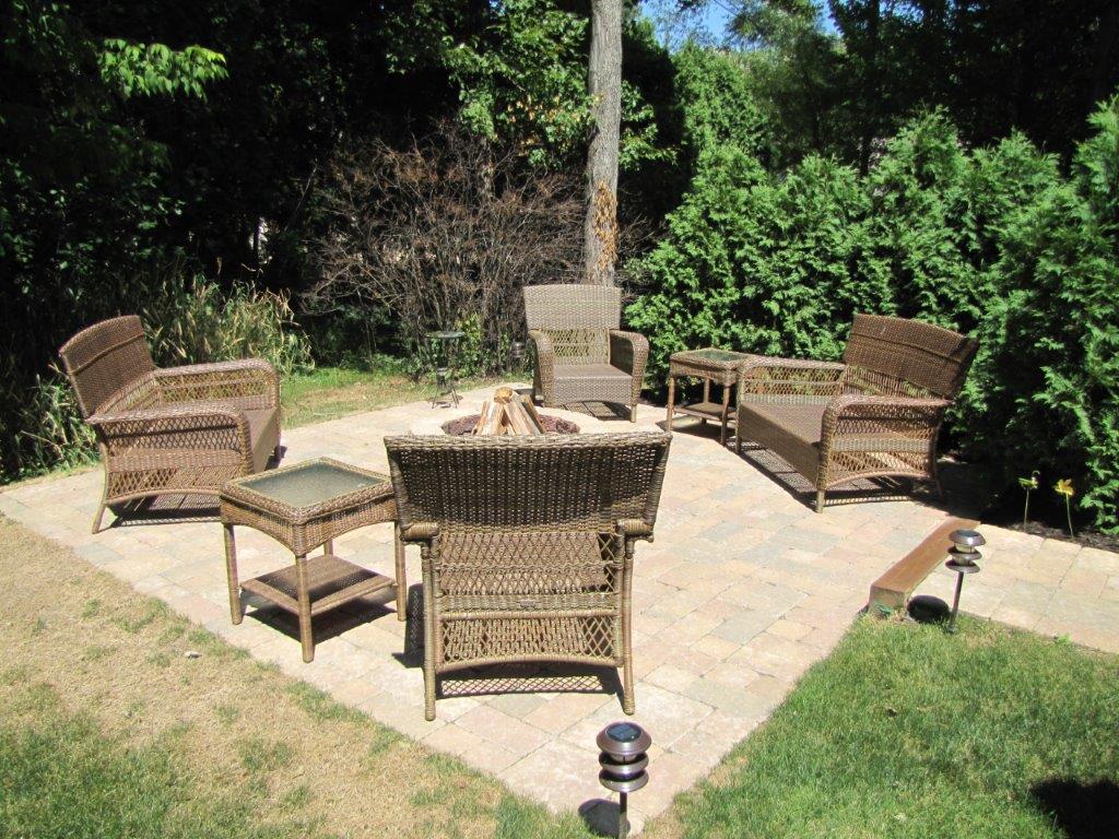 Wicker patio seating arranged around a fire pit on a sunny outdoor deck with greenery around it