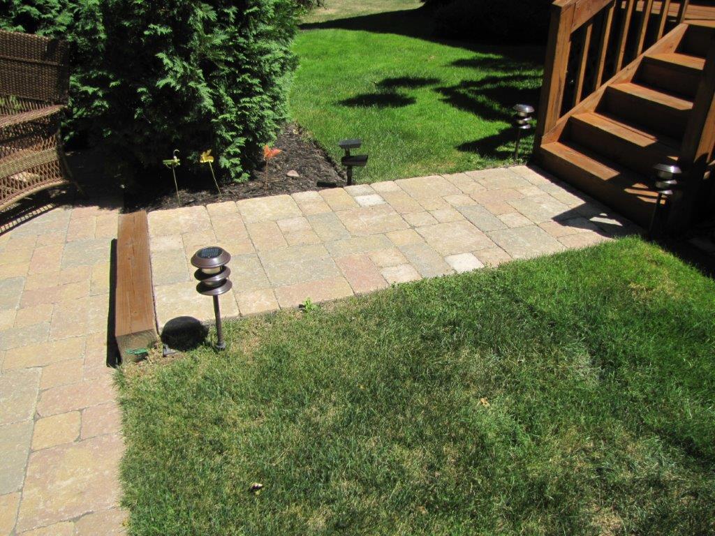 Backyard patio with stone walkway, green lawn, and wooden deck stairs