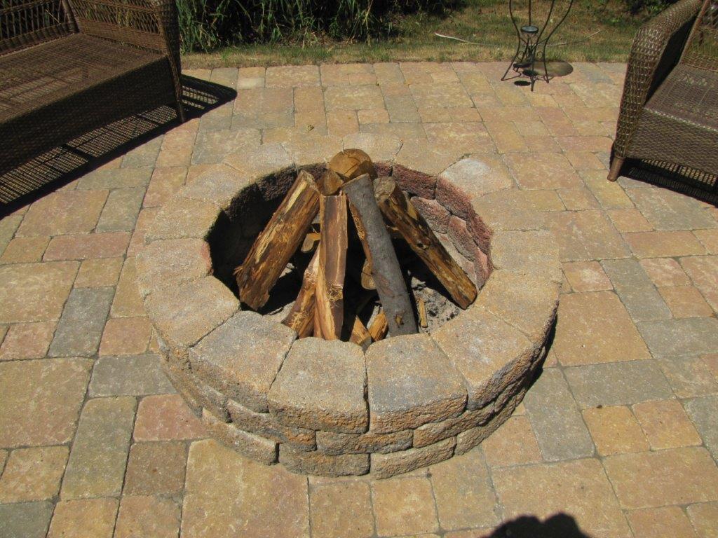 Stone fire pit with stacked logs in a paved outdoor seating area