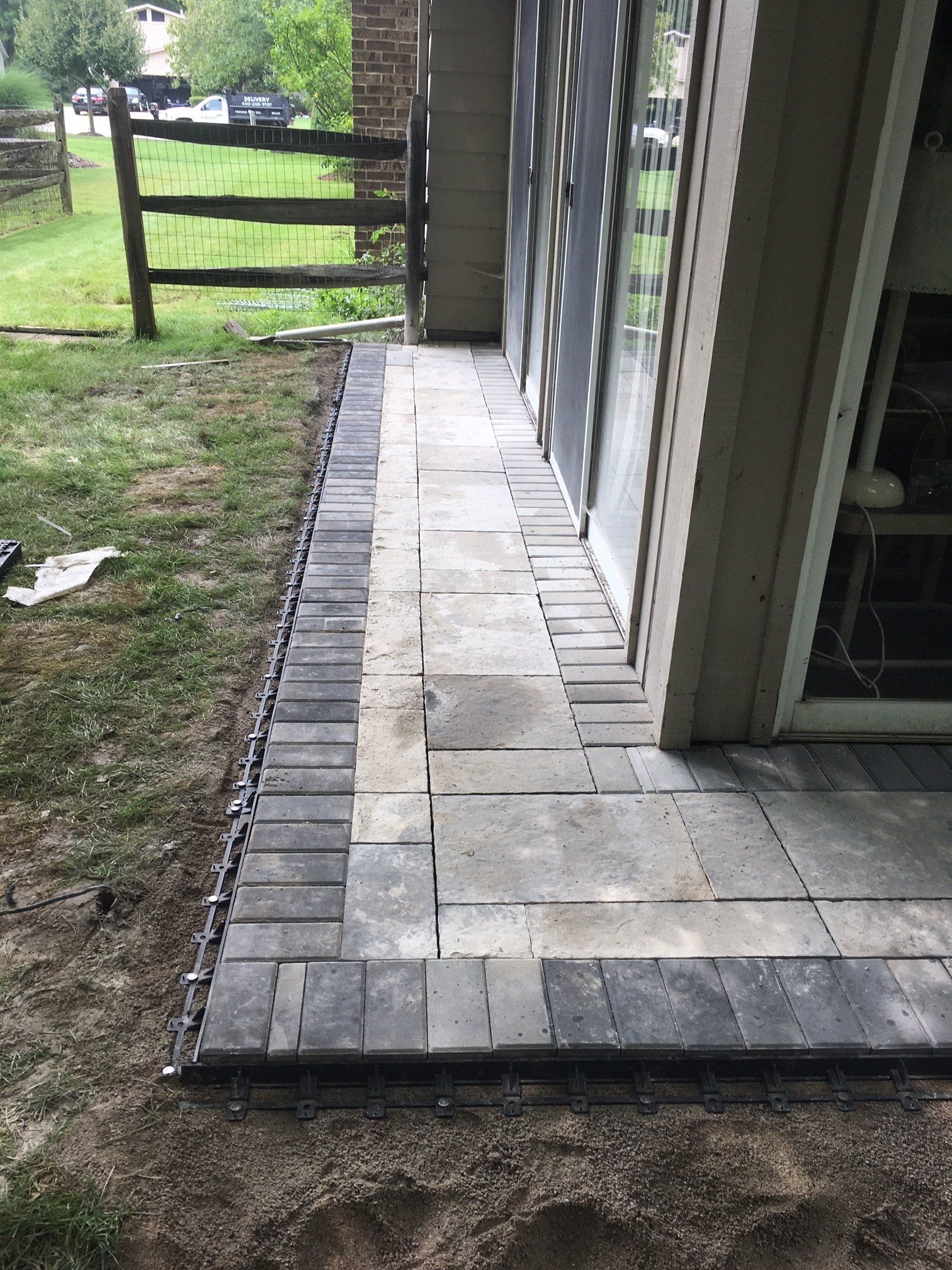 Concrete walkway beside a building with a wooden fence and grassy yard