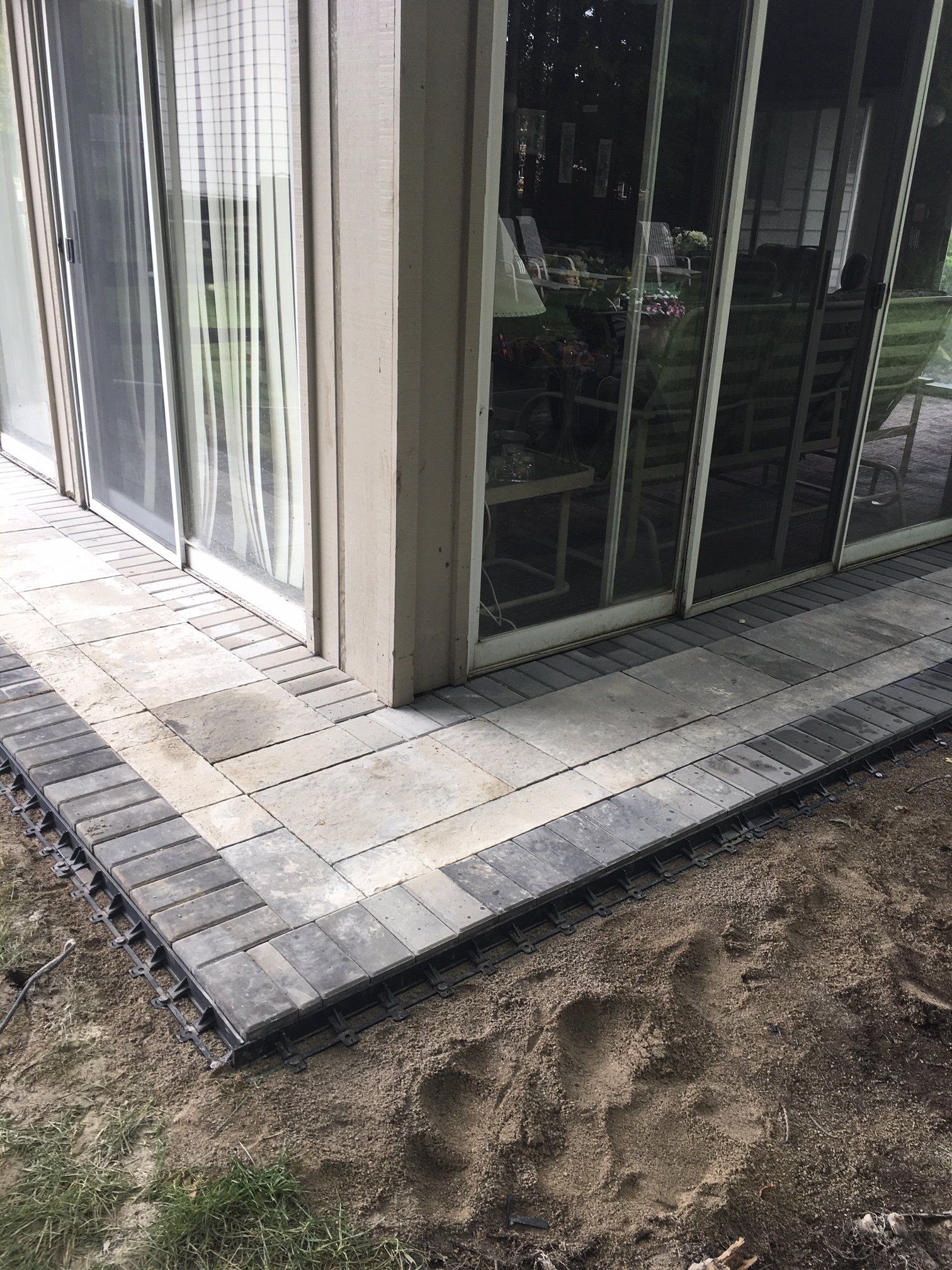 Concrete patio beside glass doors, with a dirt patch at the edge and a small step down.