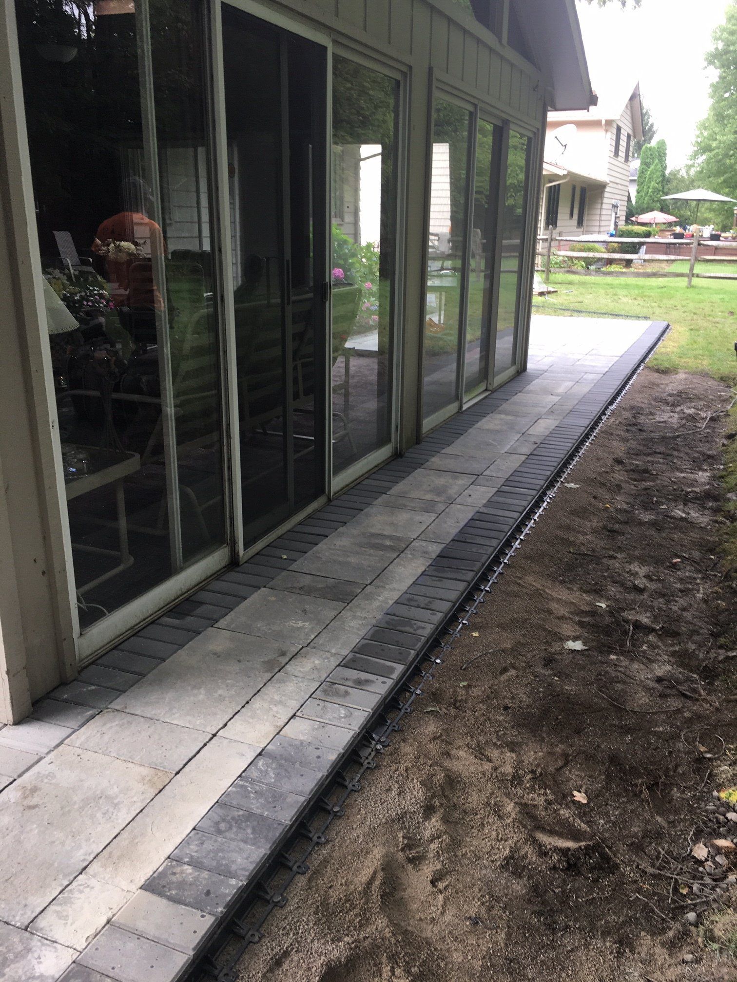 House side with sliding glass doors and a narrow paved walkway beside a dirt yard.