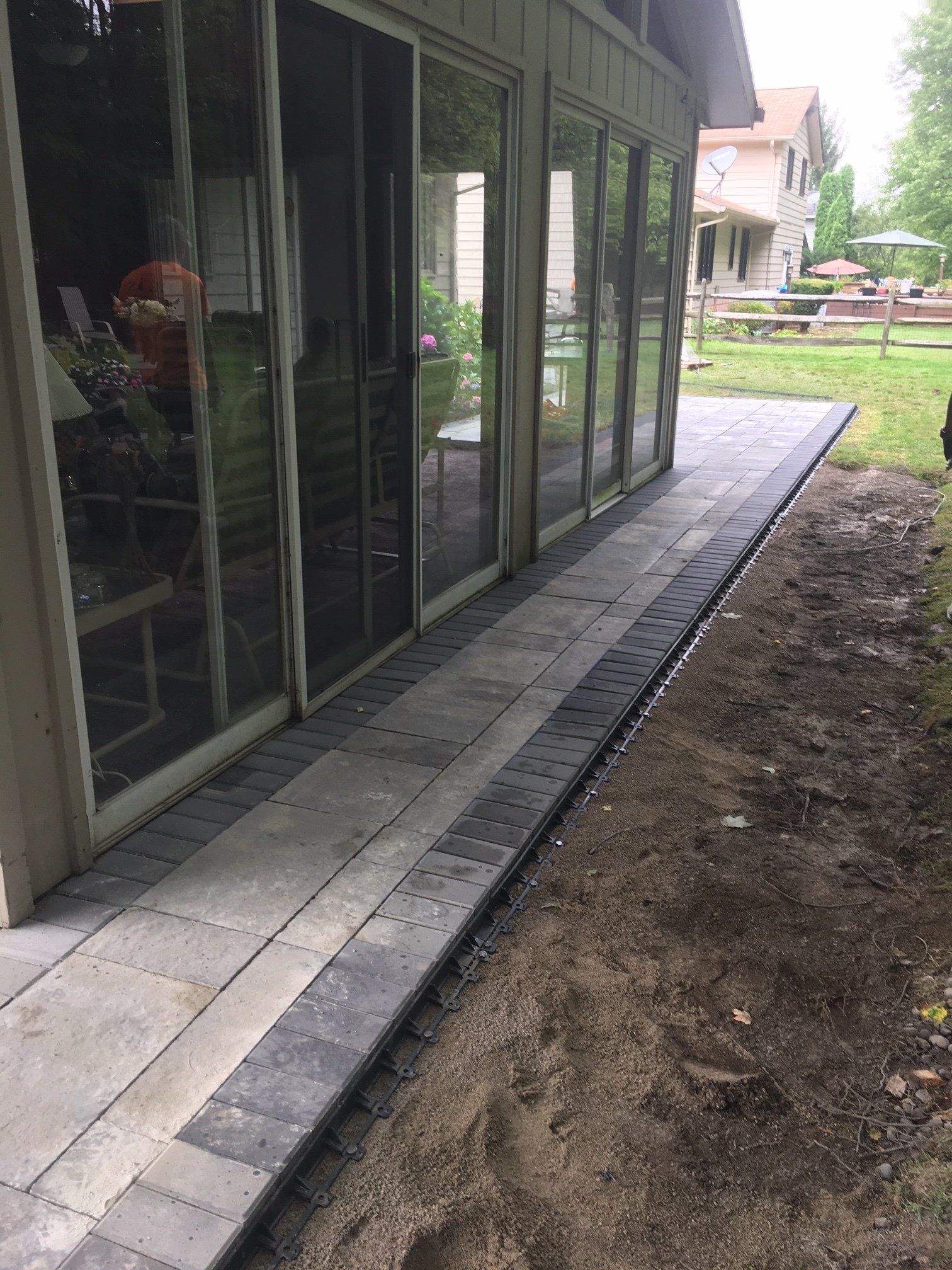 House exterior with glass doors and a narrow paved walkway beside a dirt yard