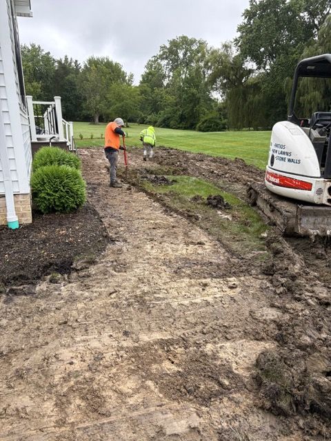 Workers digging a muddy trench beside a house, with an excavator on a grassy lawn.
