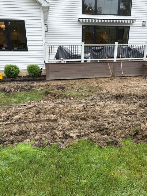 Backyard with muddy lawn, green grass edge, and a house deck with patio furniture and railing