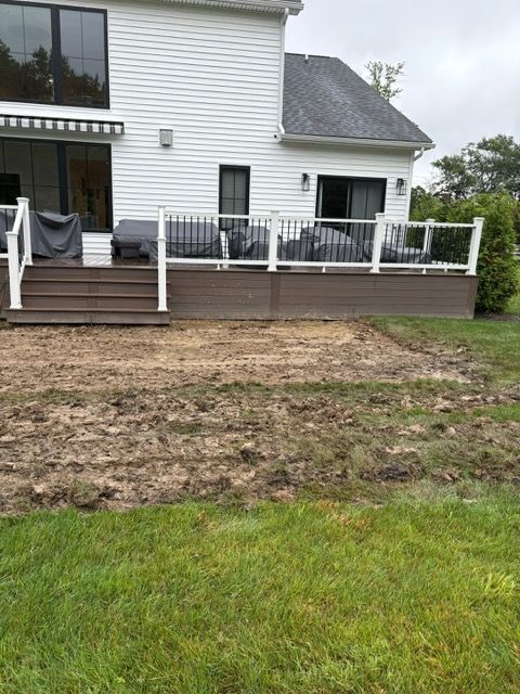 Backyard with raised wooden deck, white railing, and patchy dirt lawn in front of a white house