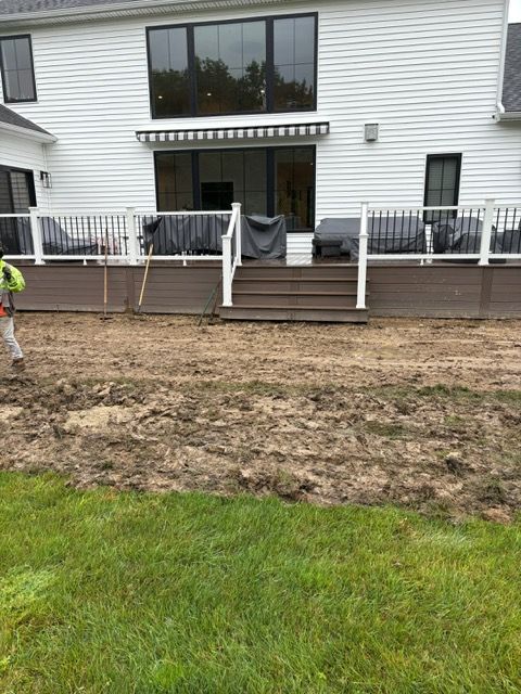 Backyard deck and patio area with muddy ground and a white house in the background