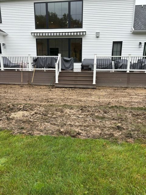 Backyard patio with deck, steps, white railing, and a muddy lawn in front of a house