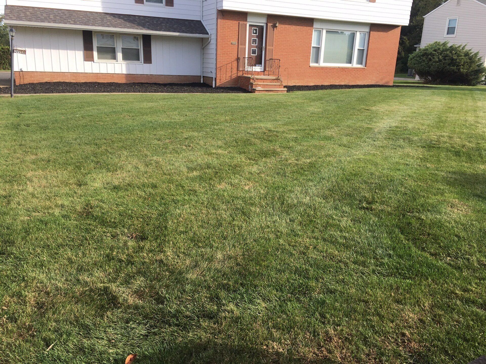 Suburban house with brick and white siding behind a large green front lawn