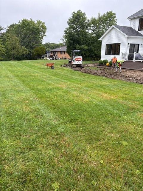 Freshly mowed suburban lawn beside a white house with flower beds and trees under cloudy skies