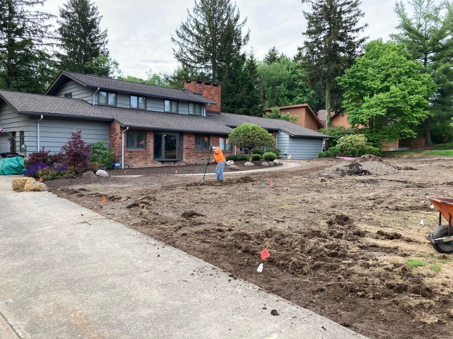 House and garage beside a muddy yard, with a child standing near the center and tall trees behind.