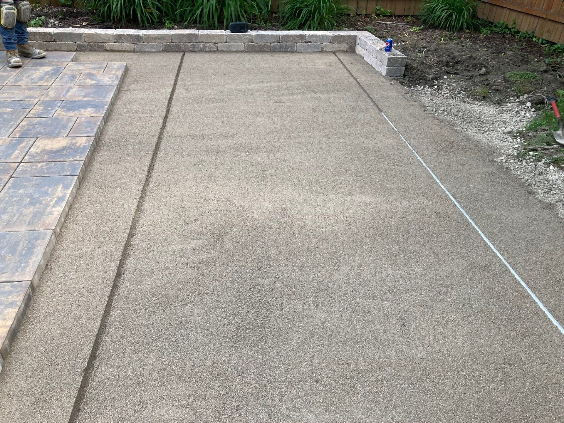 Freshly poured concrete driveway slab beside a tiled walkway and garden border