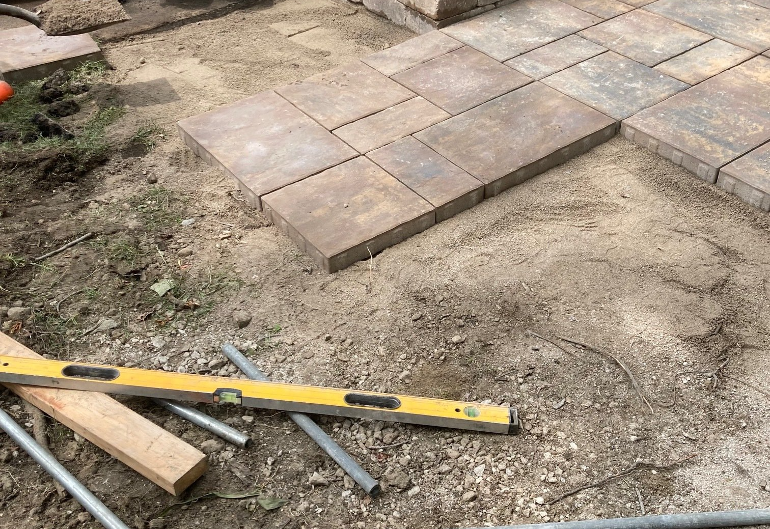 Partially installed stone pavers with tools on a dirt patio area