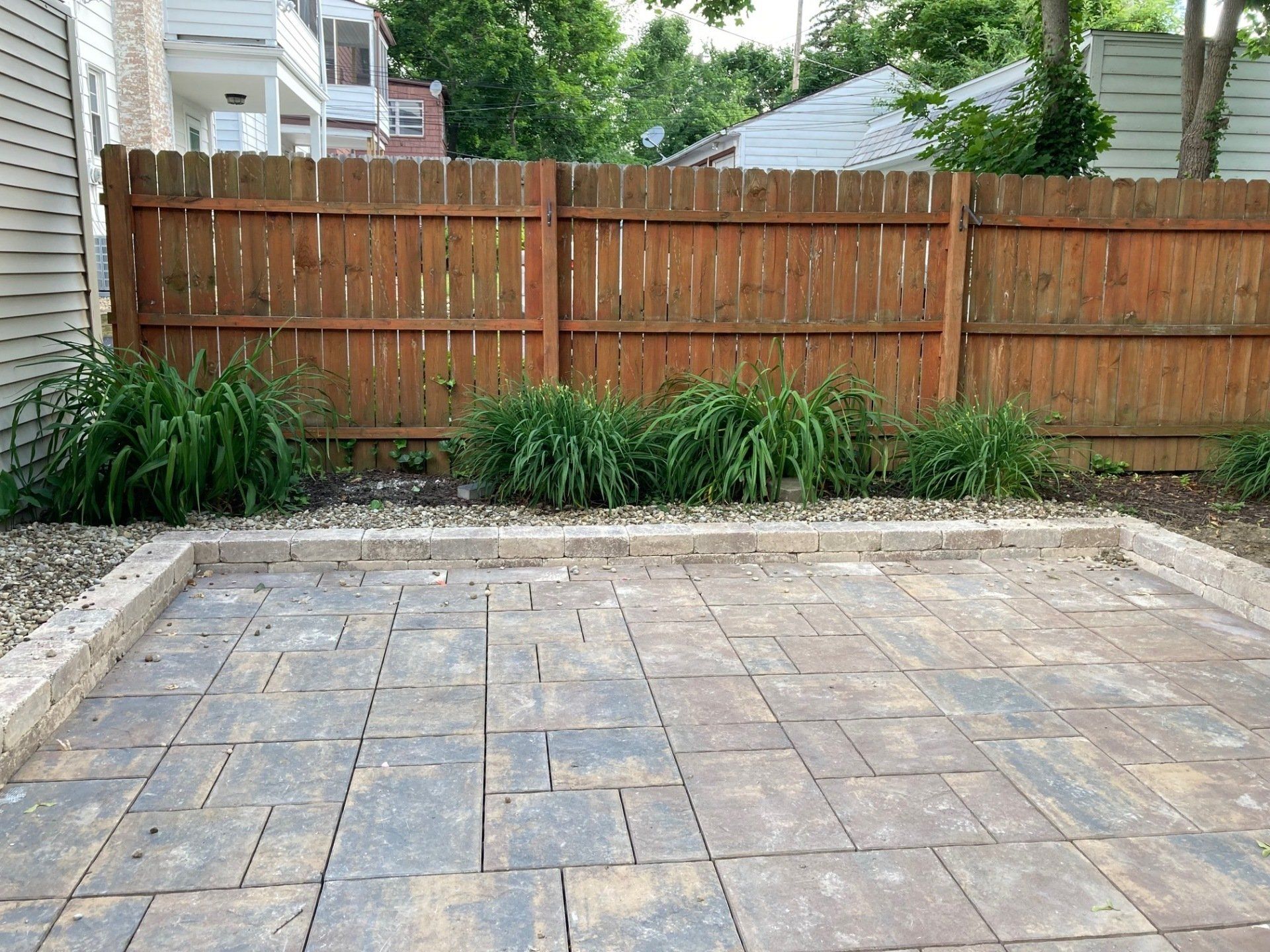 Empty stone patio with wooden fence and plants along the back edge.