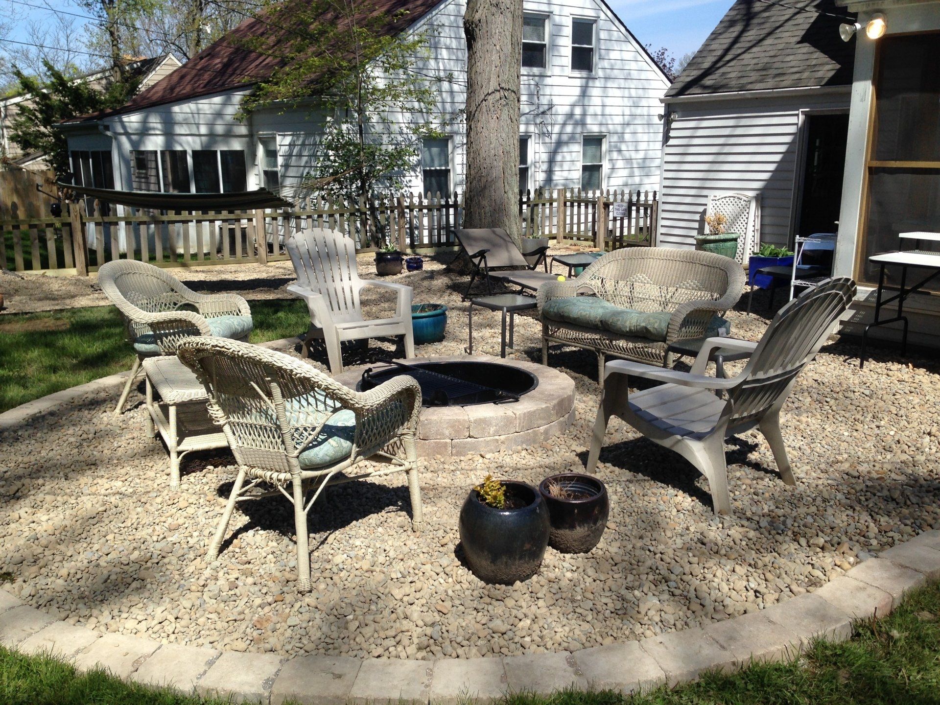 Backyard patio with a fire pit, wicker chairs, and gravel seating area beside a house
