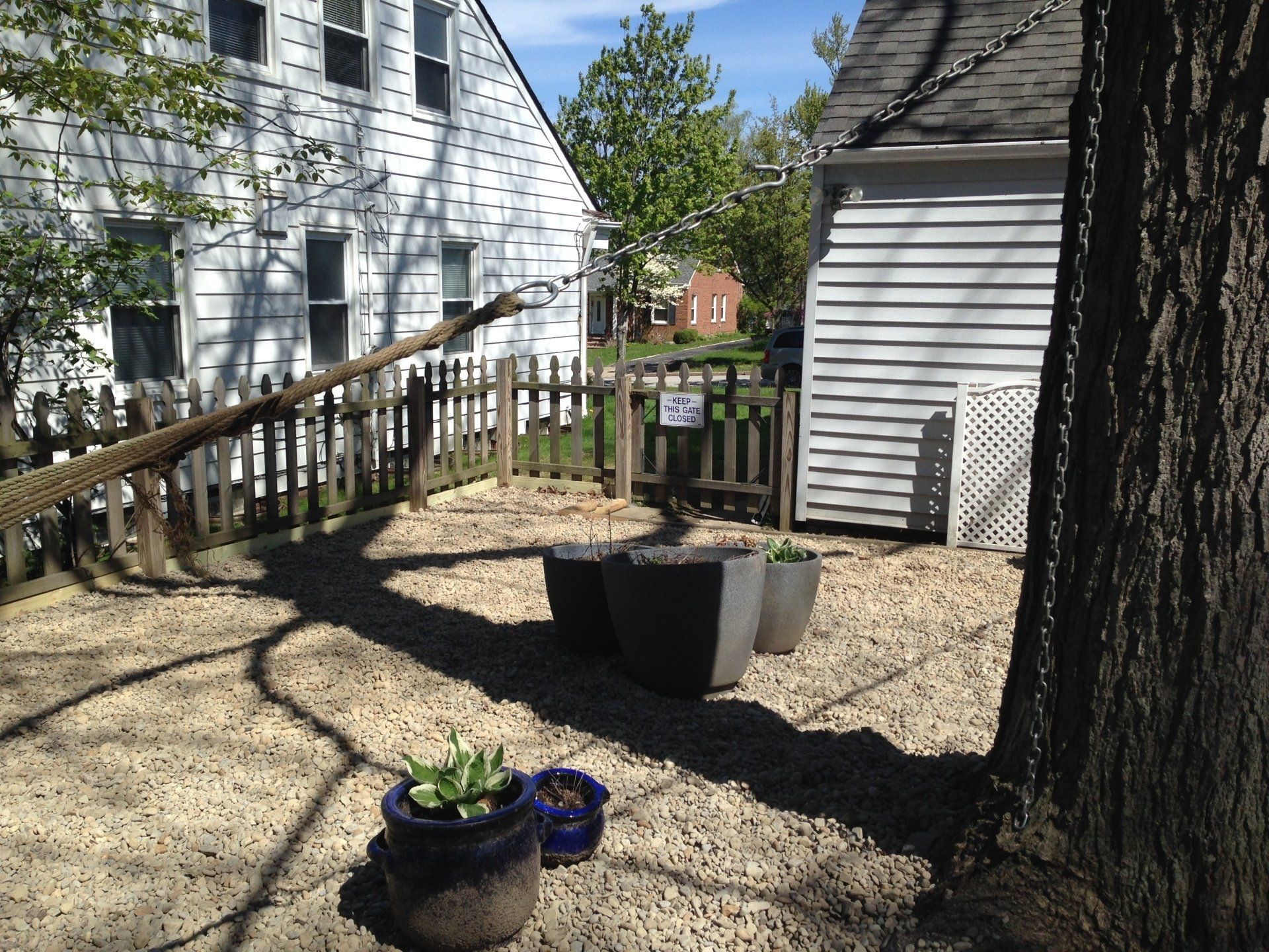 Backyard with white house, tree, picket fence, and potted flowers in gravel yard