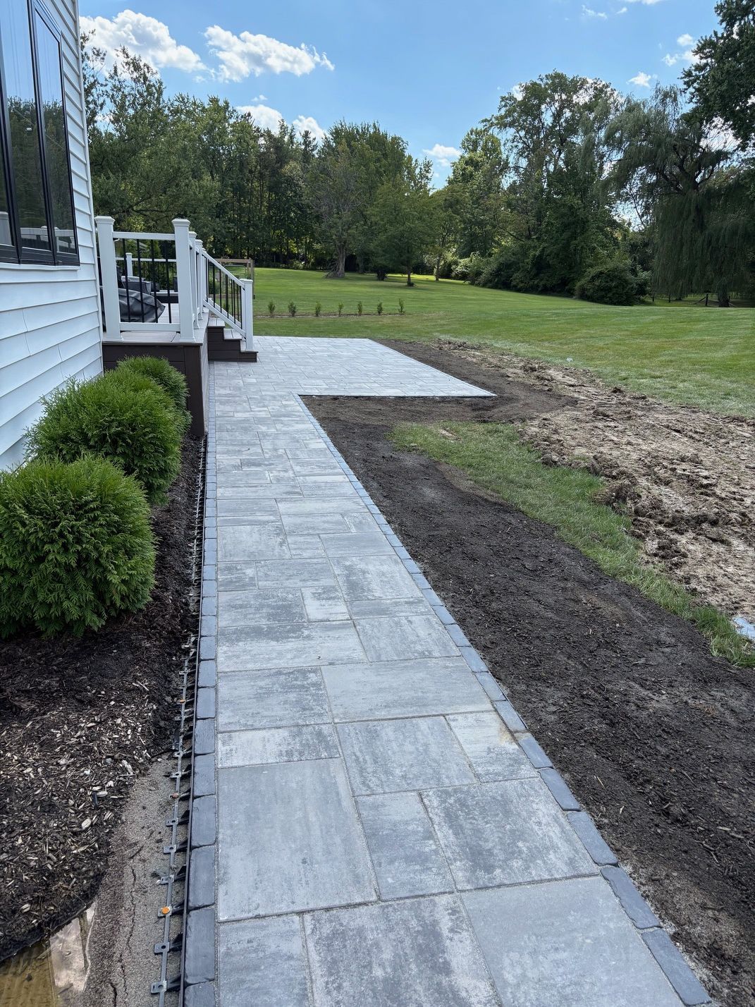 Stone walkway along a white house leading to a grassy yard and trees