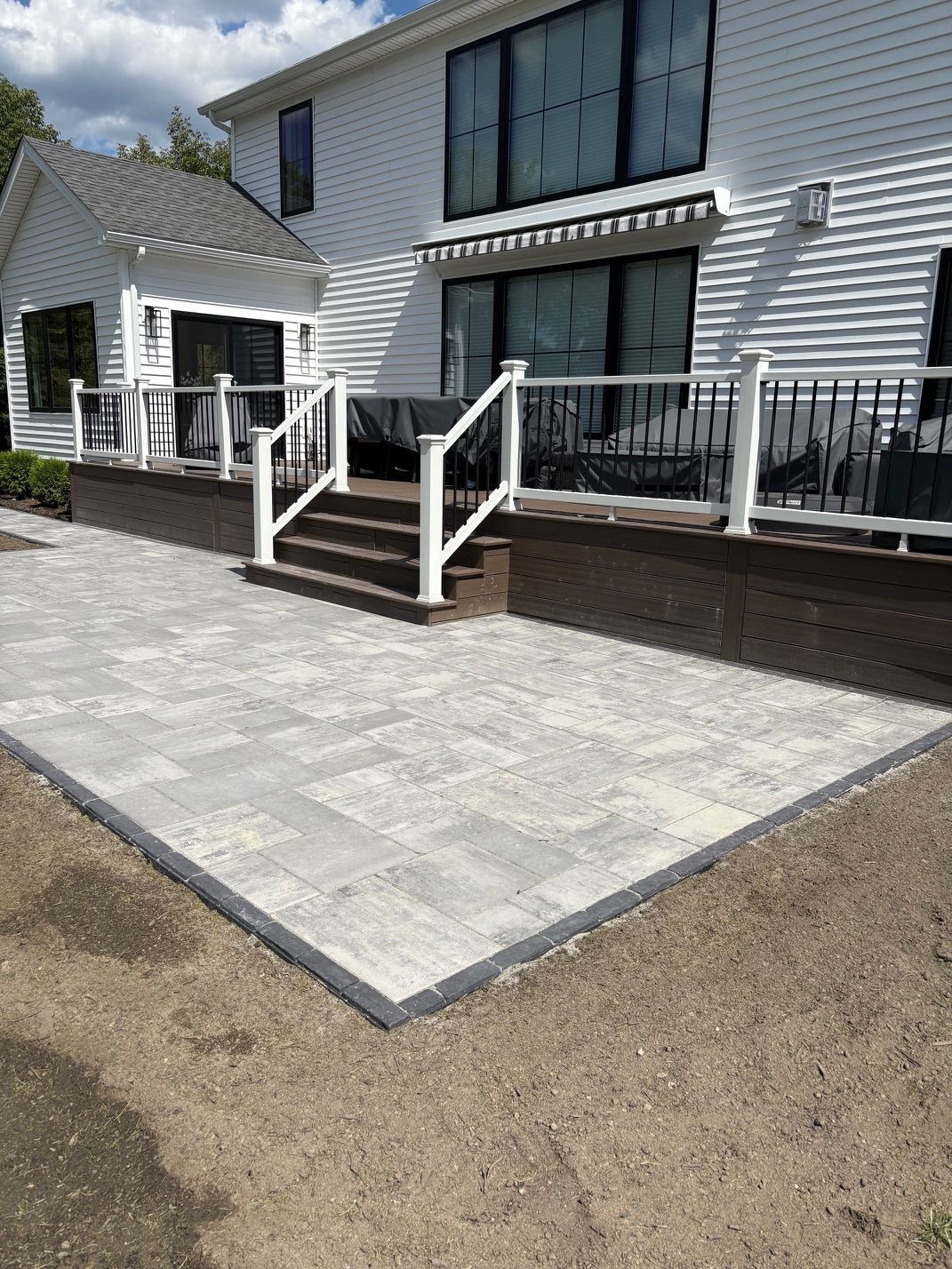 Backyard patio with gray pavers, white railing, and steps leading to a house