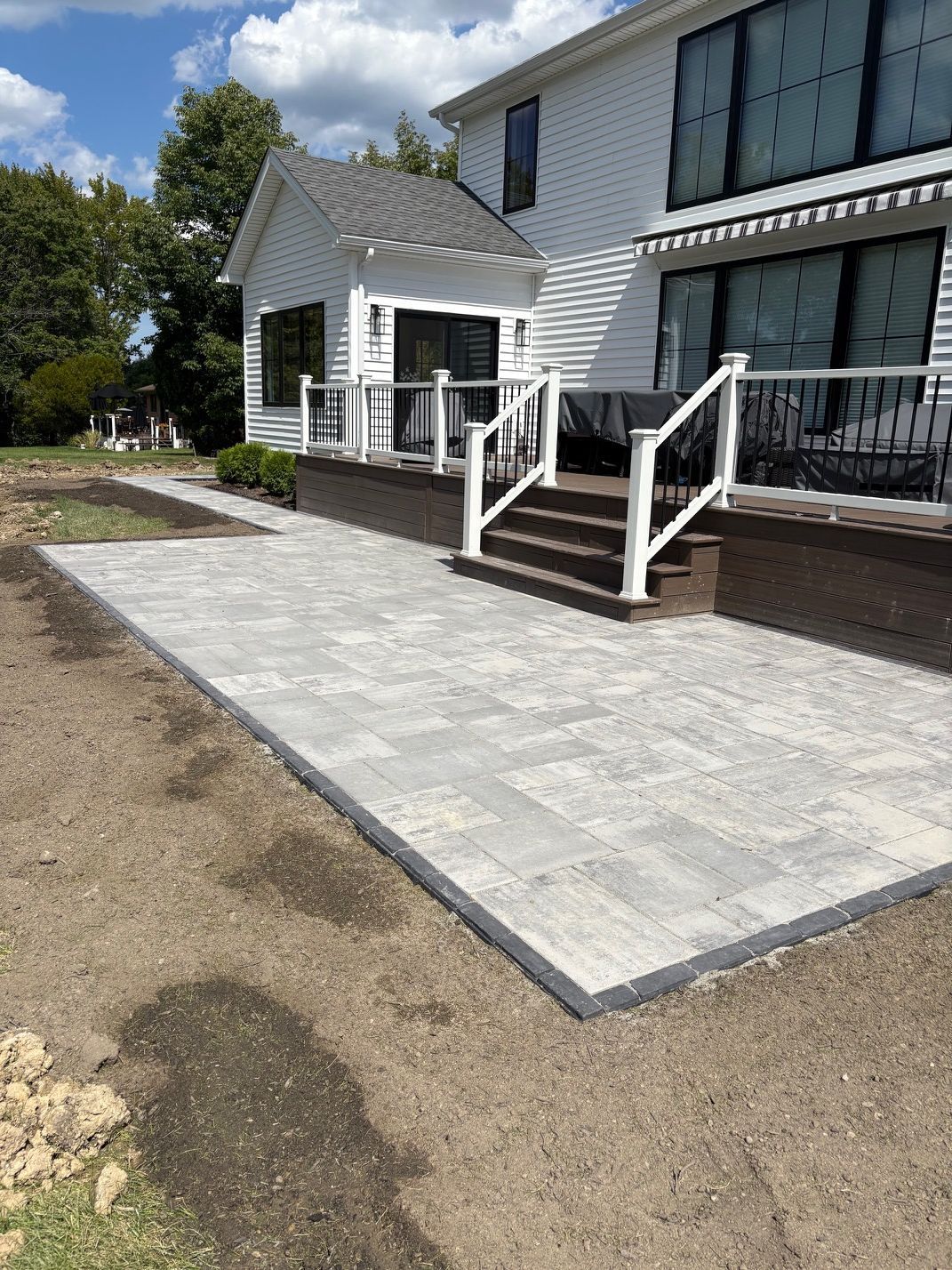 New concrete patio beside a house with white railings and steps under a sunny sky