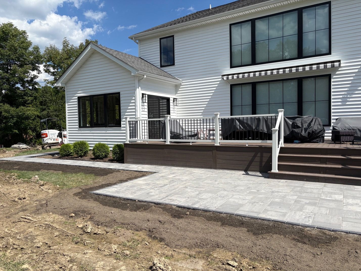 Modern two-story house with a large patio, deck railings, and a paved walkway in front