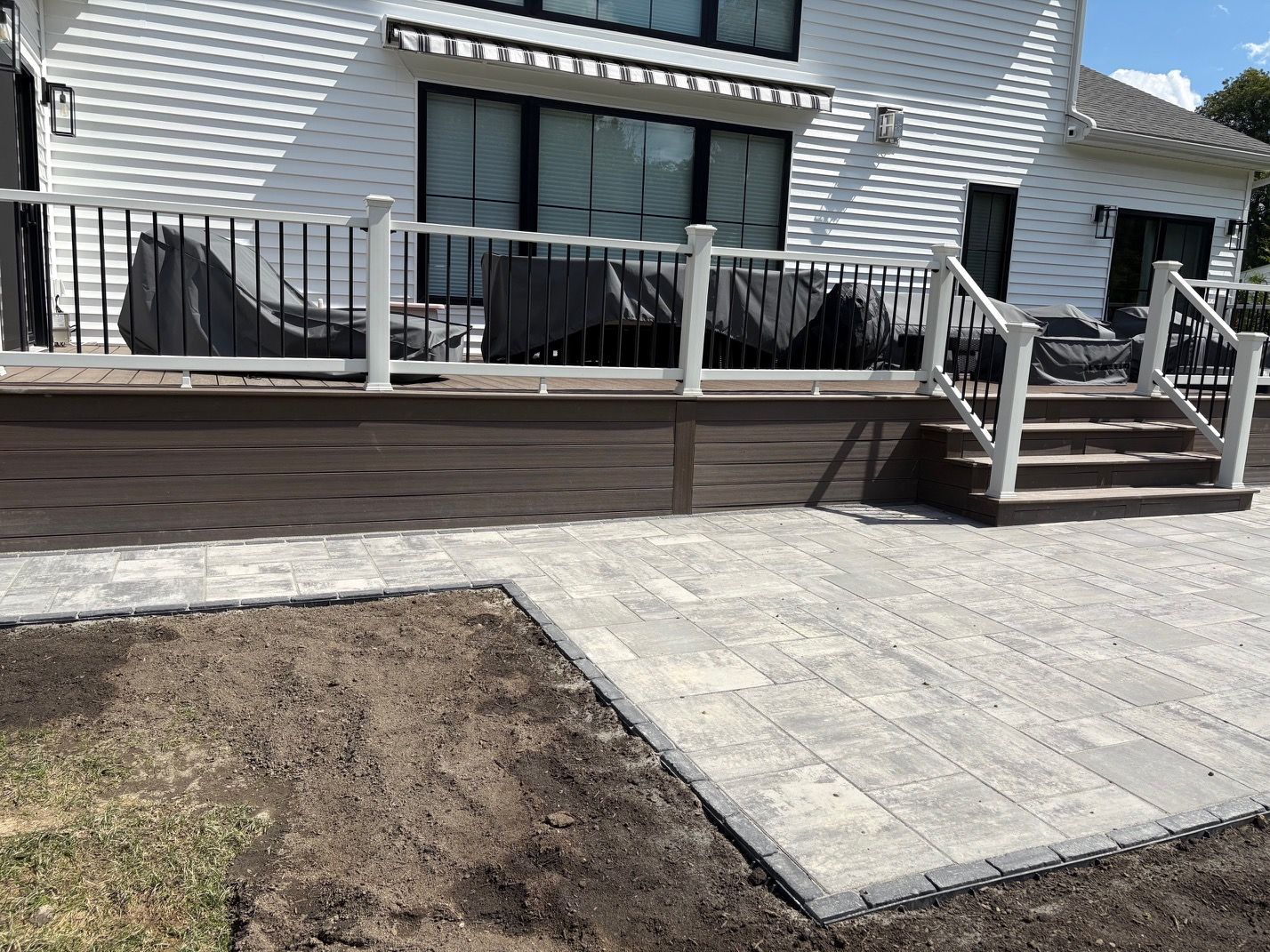 Back deck with white railing, outdoor furniture, and stone paver patio beside a small lawn area