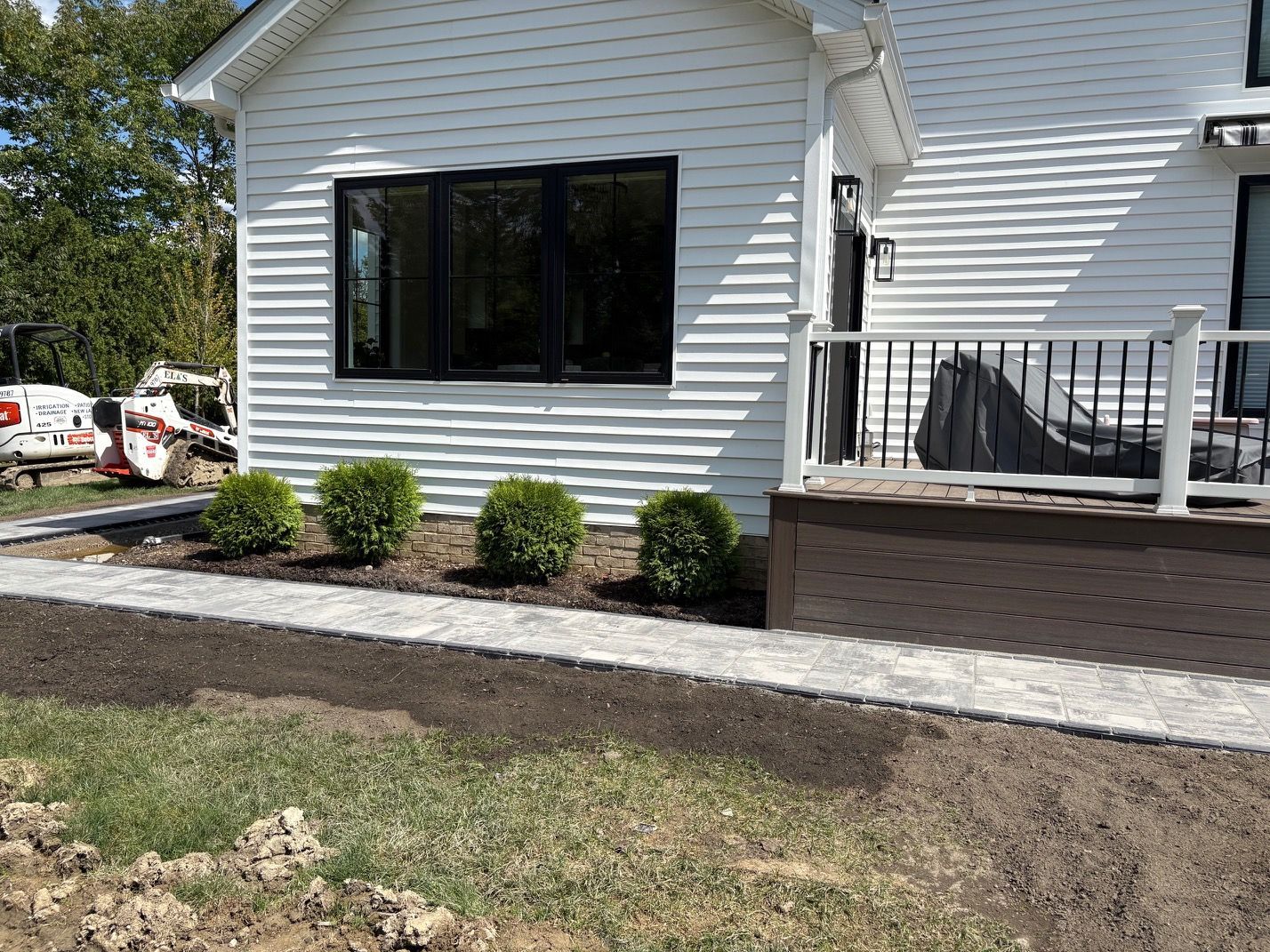 Front of a white house with black window, small shrubs, and a raised deck with railing