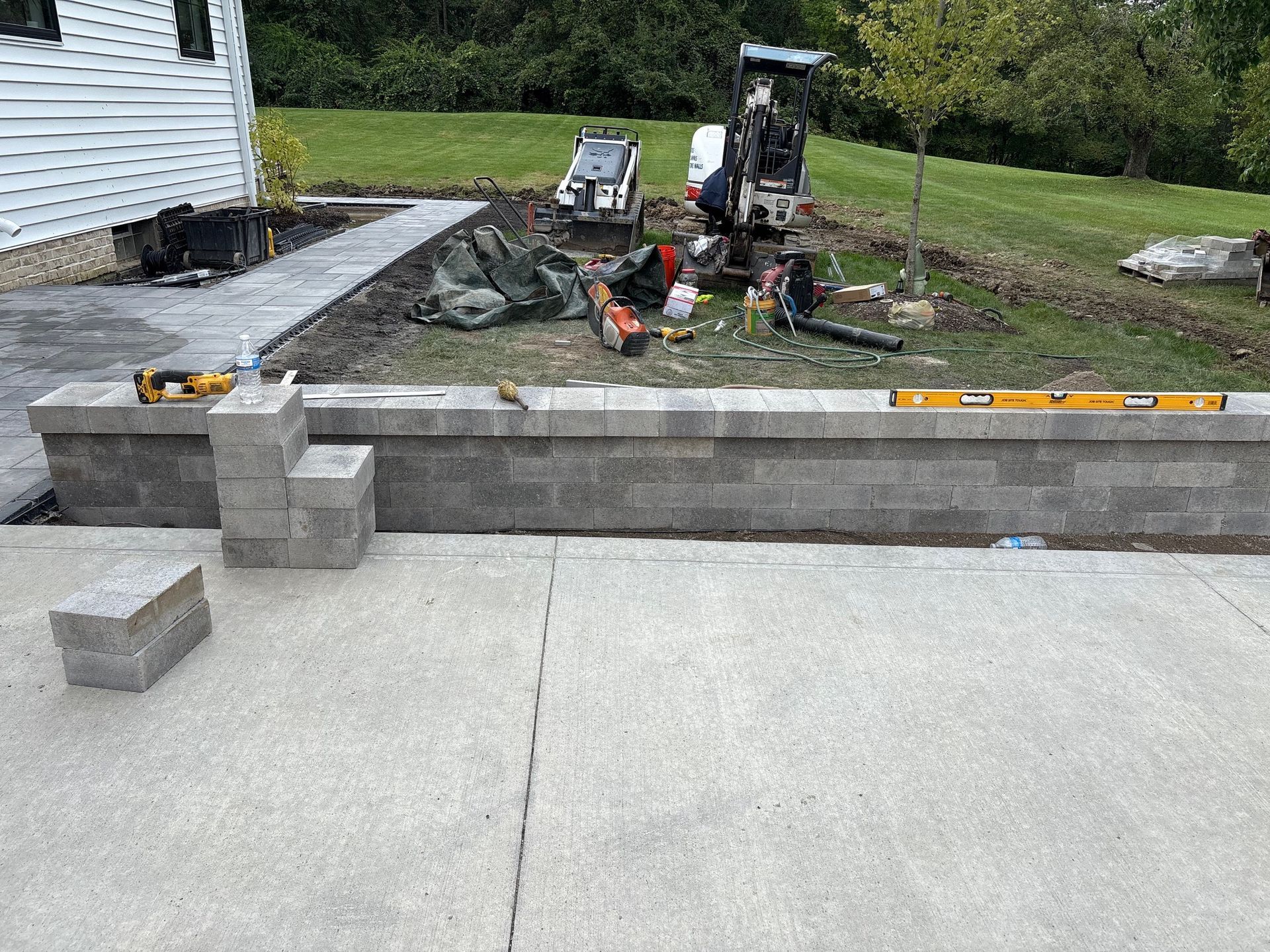 Driveway under construction with stacked concrete blocks, tools, and a grassy yard in the background.