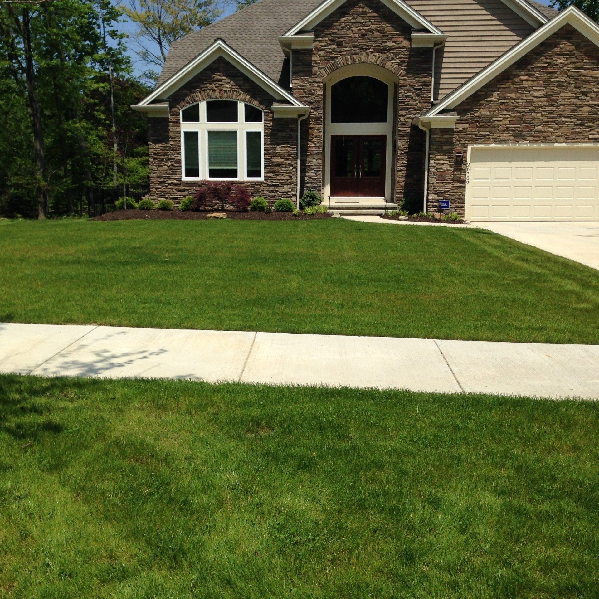 Suburban brick house with manicured lawn, front walkway, and attached garage on a sunny day