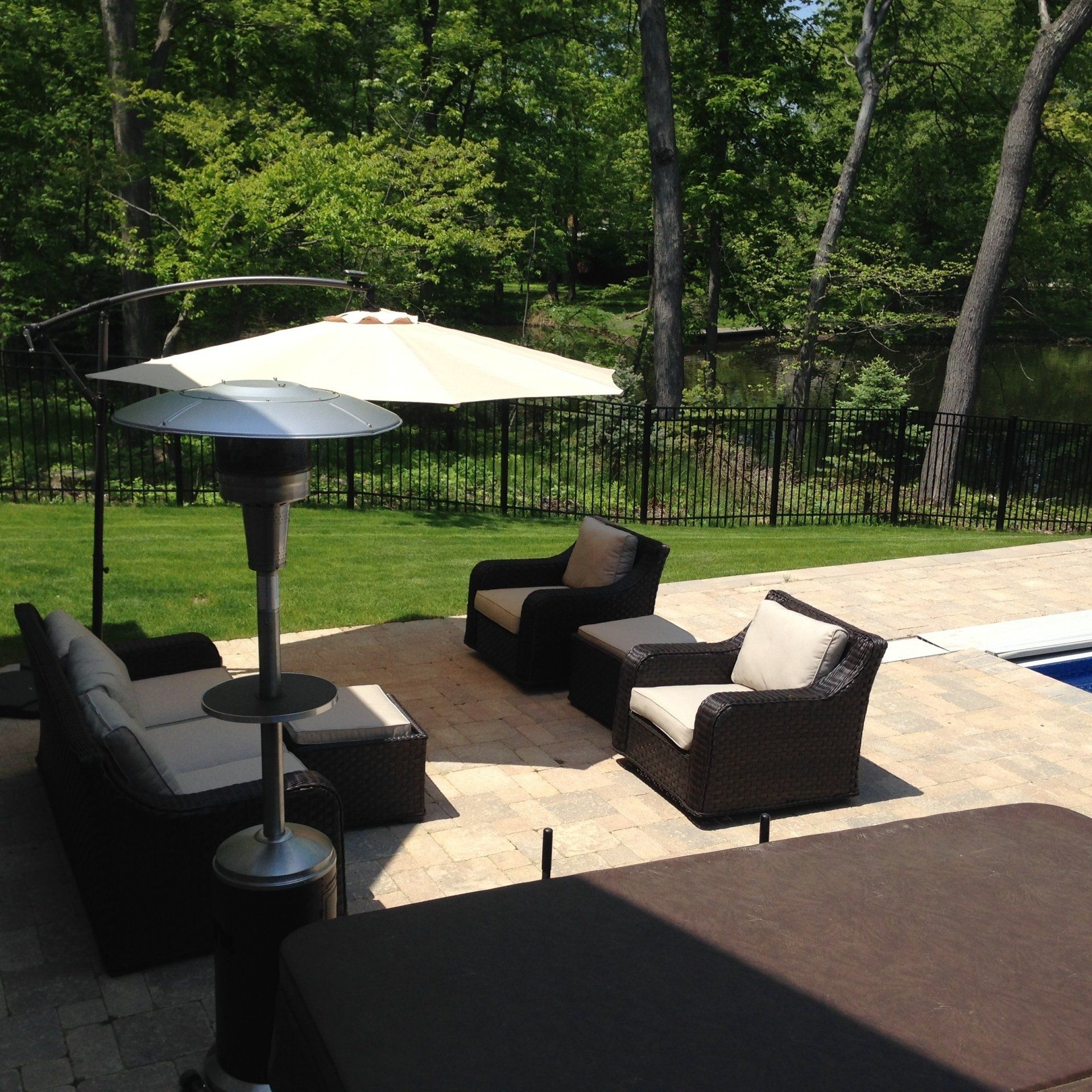 Patio with wicker chairs, table umbrellas, and a pool beside a green backyard with trees