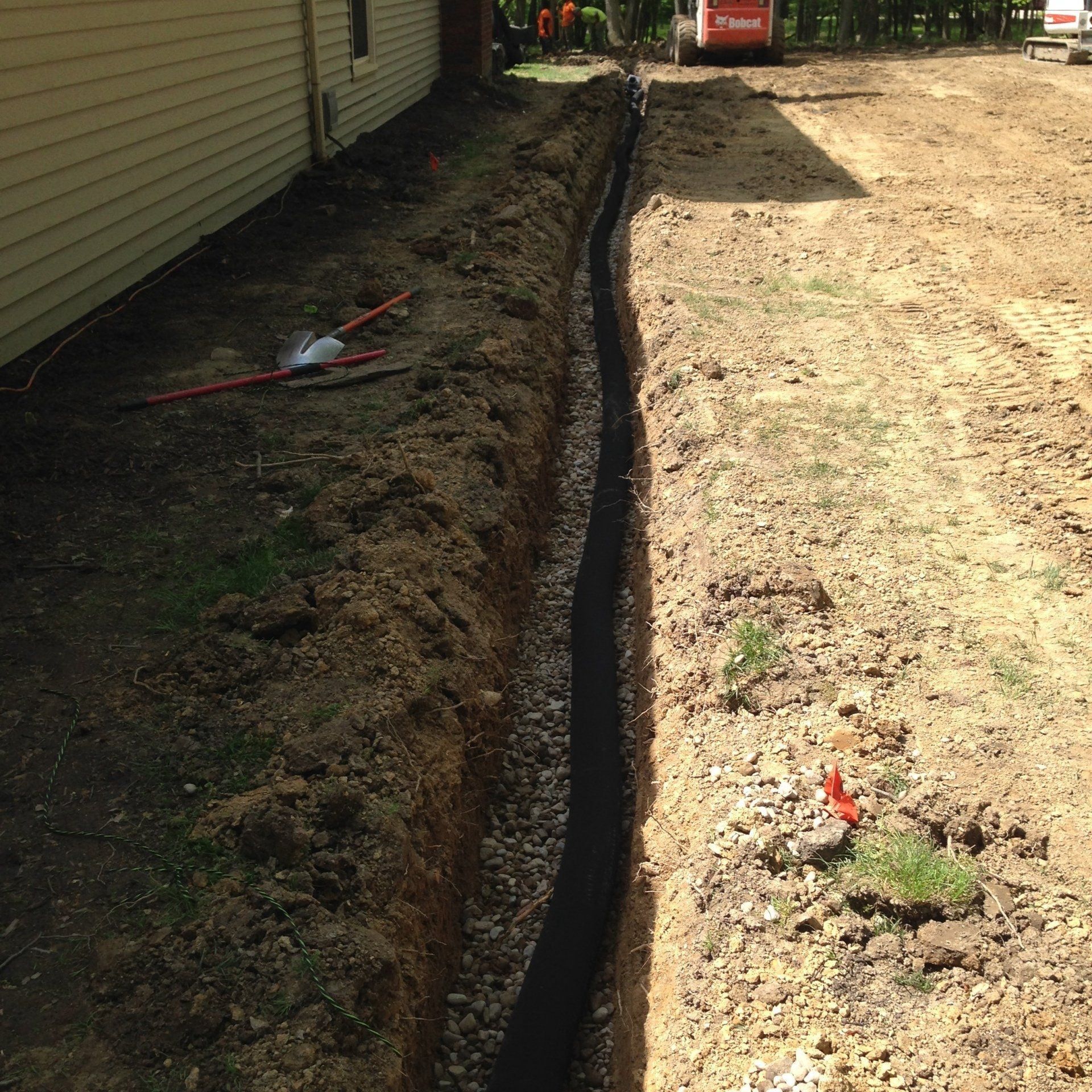Trenched yard beside a house, with a narrow ditch separating dark soil from a gravel path.