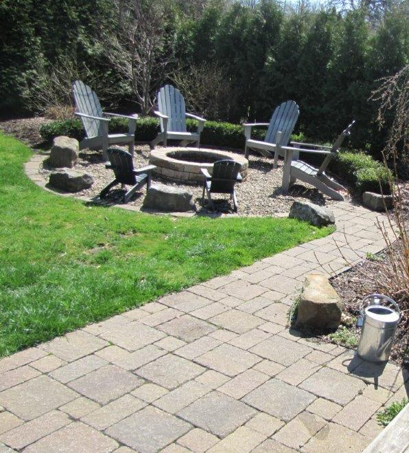 Backyard patio with stone fire pit, Adirondack chairs, and a curved paver walkway